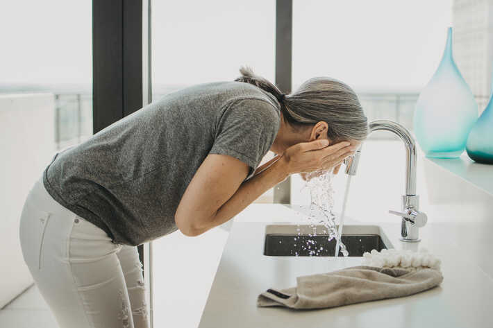 a woman washing her face in a white room with bright light