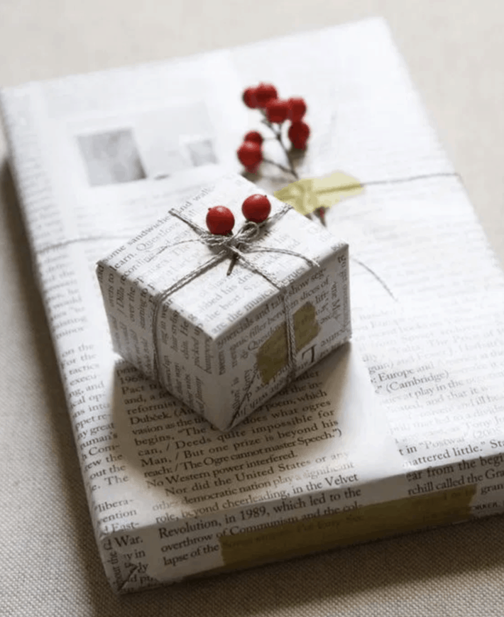 two gifts wrapped in newspaper adorned with red berries