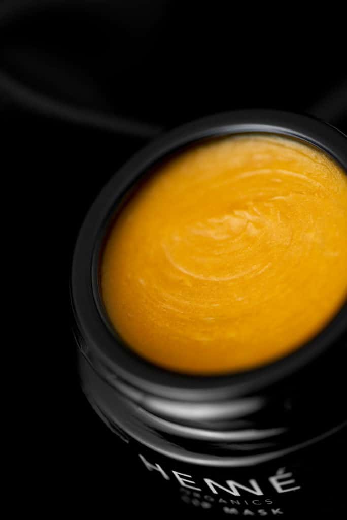 a close up of a rich yellow balm in a black jar