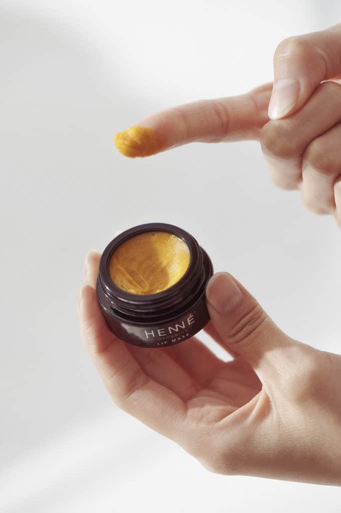 scooping a yellow colored lip mask out of a small black jar