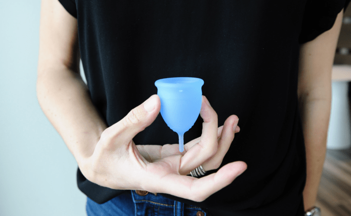 woman holding up a blue menstrual cup
