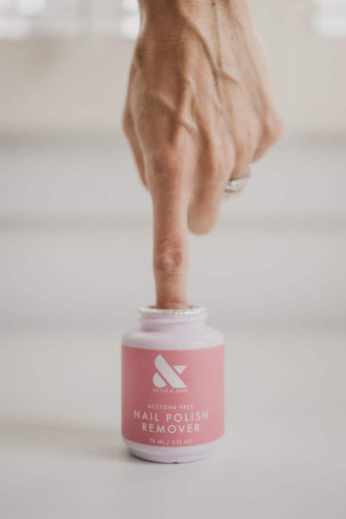 a woman sticks her pointer finger into  a jar of nontoxic olive & june nail polish remover