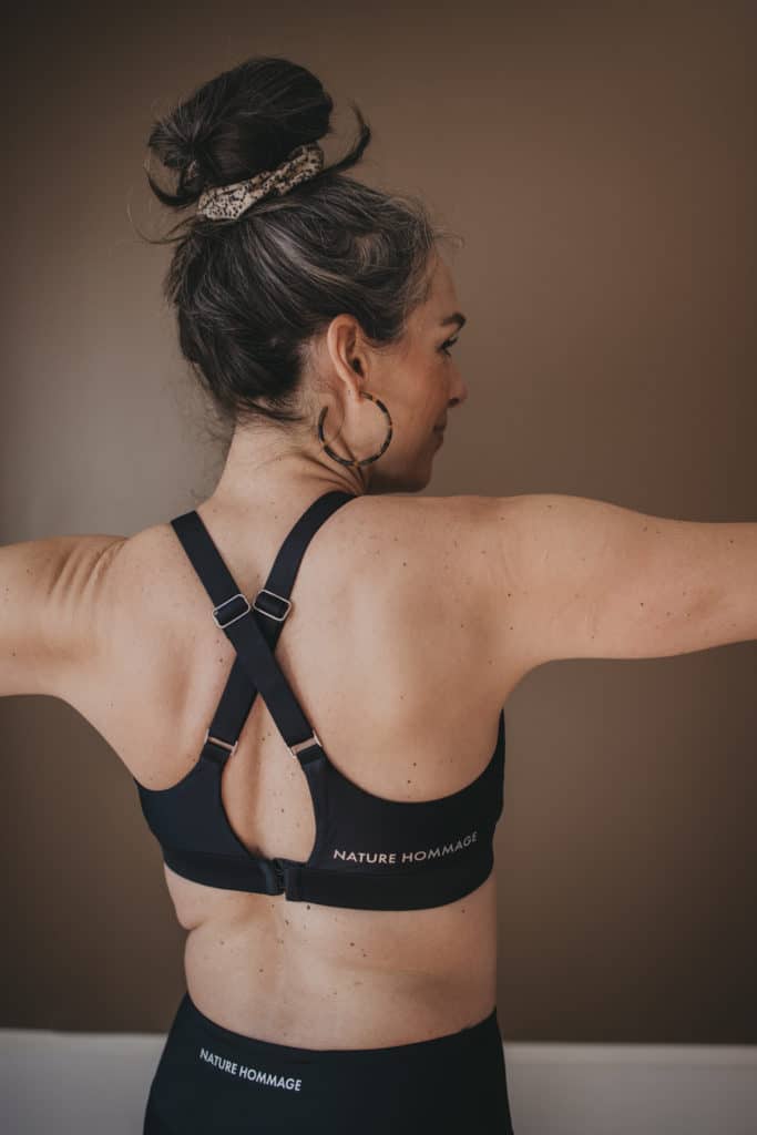 Lisa wearing a sports bra and leggings, facing away, doing a yoga pose