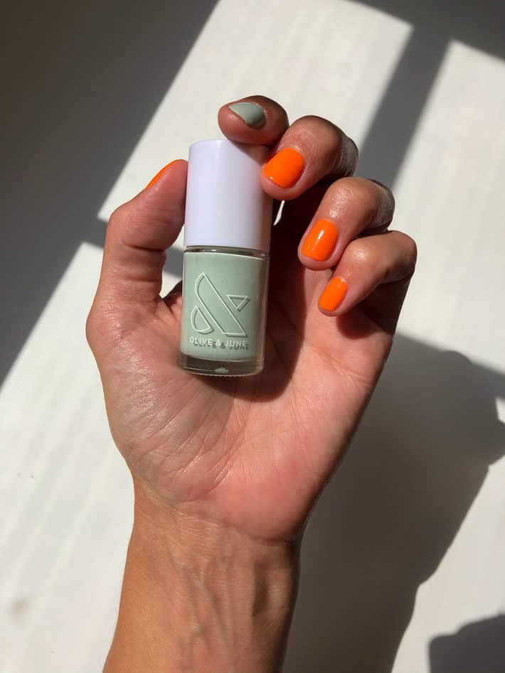 A woman shows off her orange and light teal manicure.