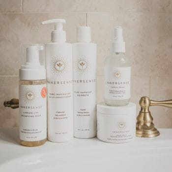 A stacked collection of Innersense hair products sits on a white bathroom sink.