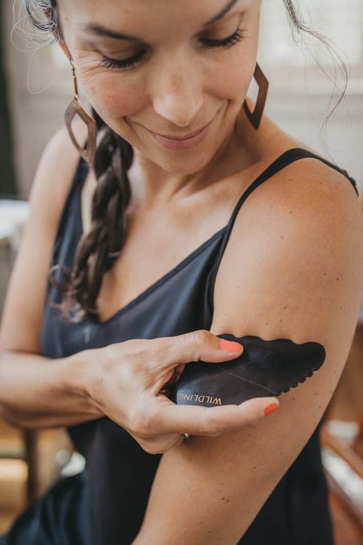 A woman uses a black gua sha stone on her arm.