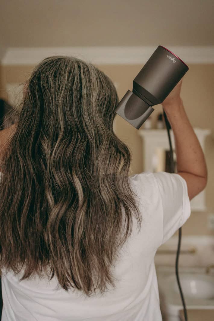 Woman with gray hair using Dyson hair dryer on curly hair