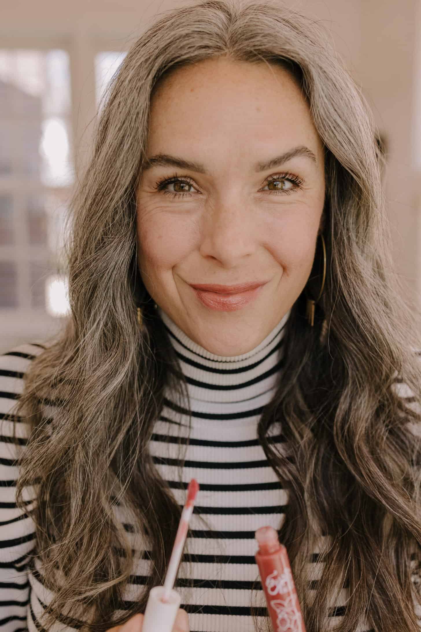 a woman holding a tube of lip gloss in her hand and smiling with the gloss on her lips