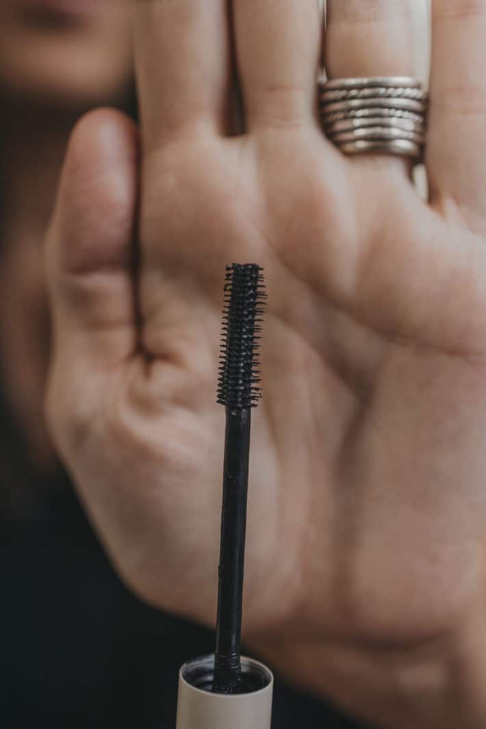 a mascara wand is held in front of a hand