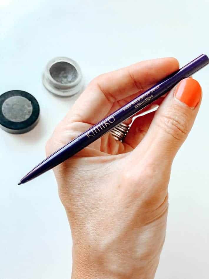 A hand with painted fingernails holds an eyebrow pencil