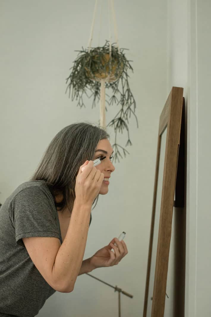 woman looks into mirror while applying mascara