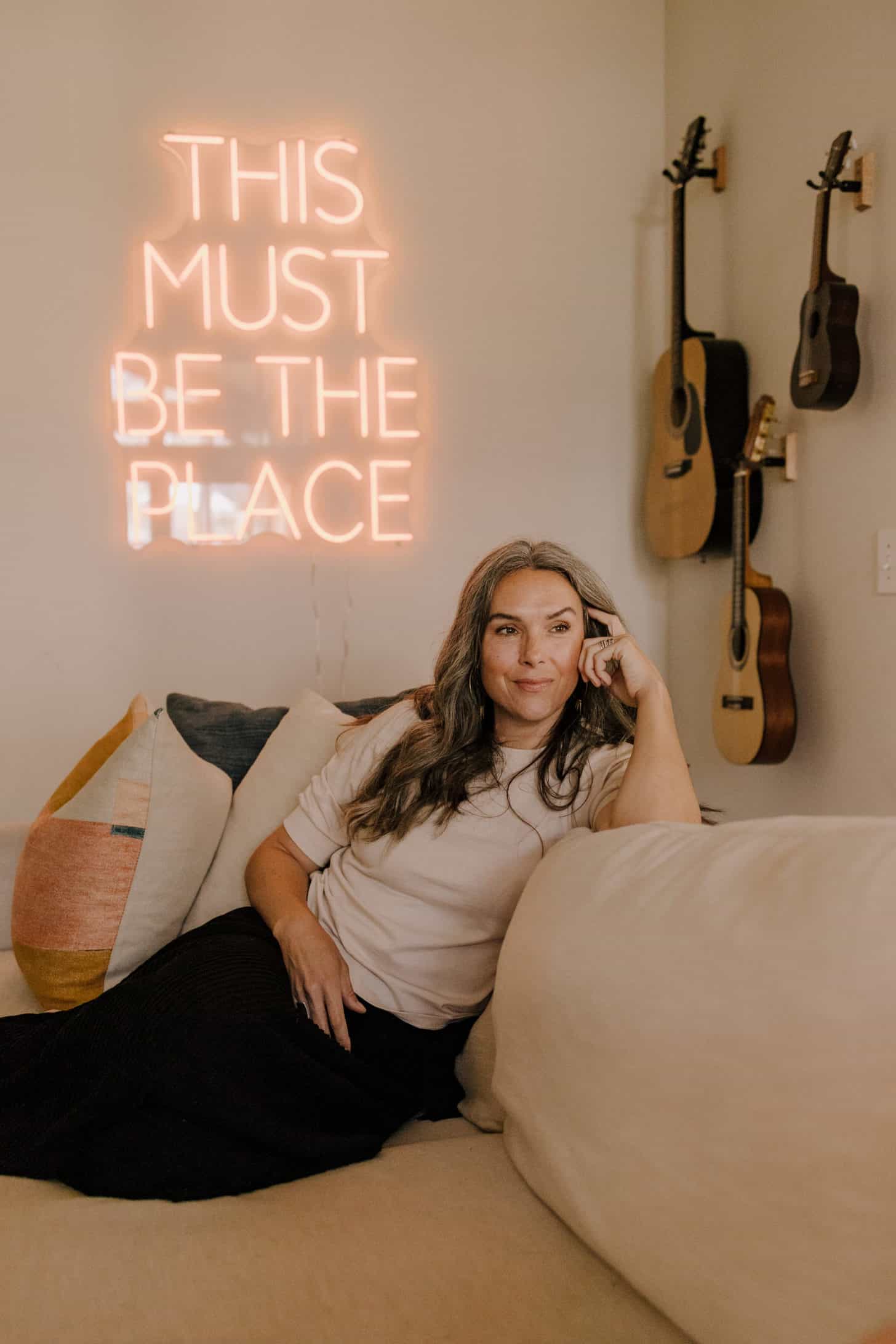 a woman sits in her living room with guitars on the wall behind her