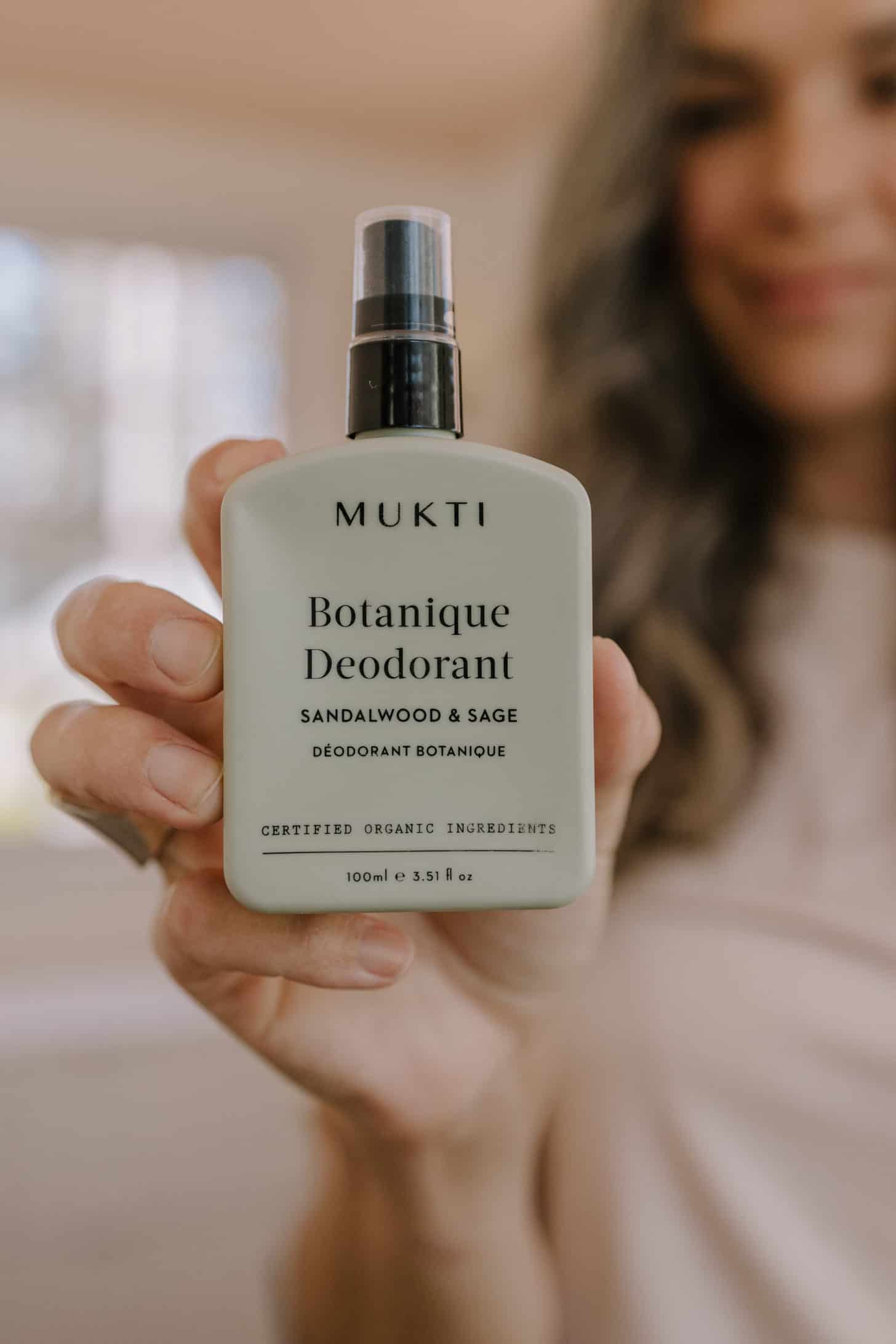 a woman holding a bottle of mukti deodorant in a green container