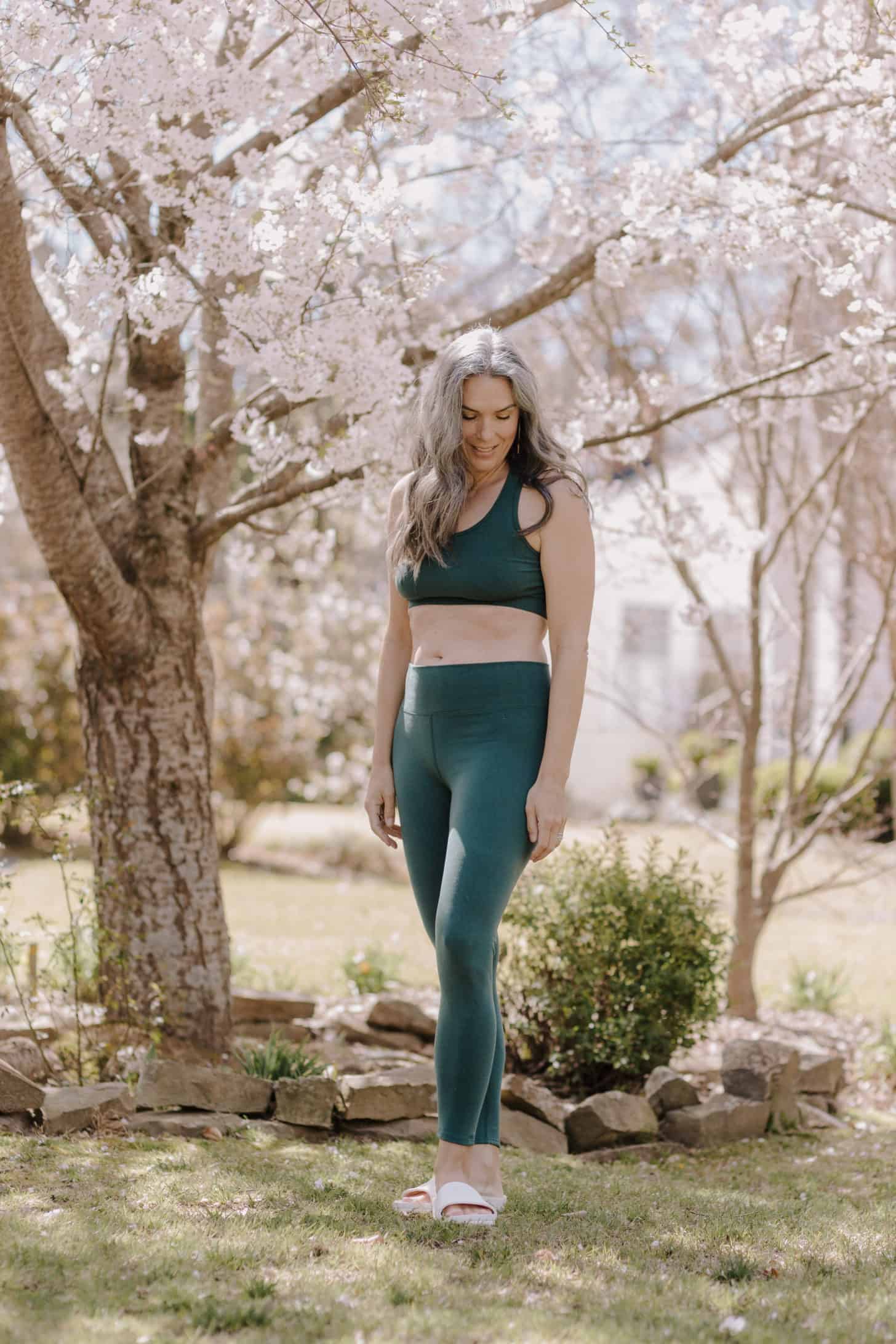 a woman standing amongst flowering trees while wearing a green pair of leggings and a crop top