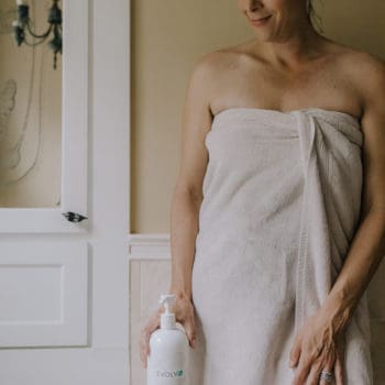 a woman stands near a bathtub holding a bottle of shampoo