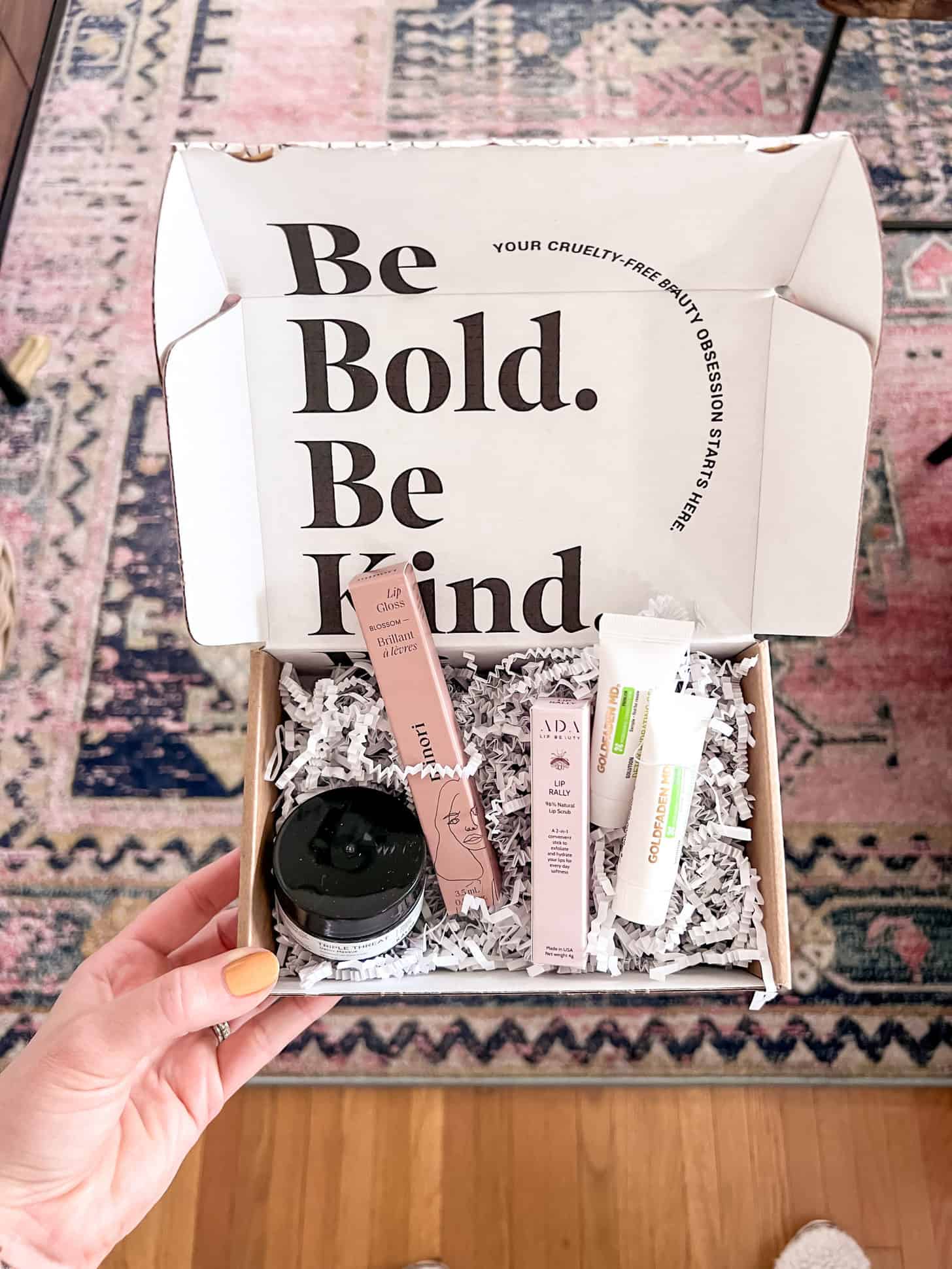 A box of clean beauty supplies is held in front of a colorful rug