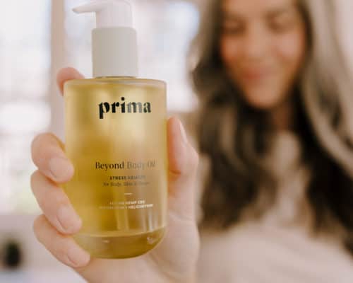 a bottle of prima is forefront in the photo with a woman standing in the background holding it