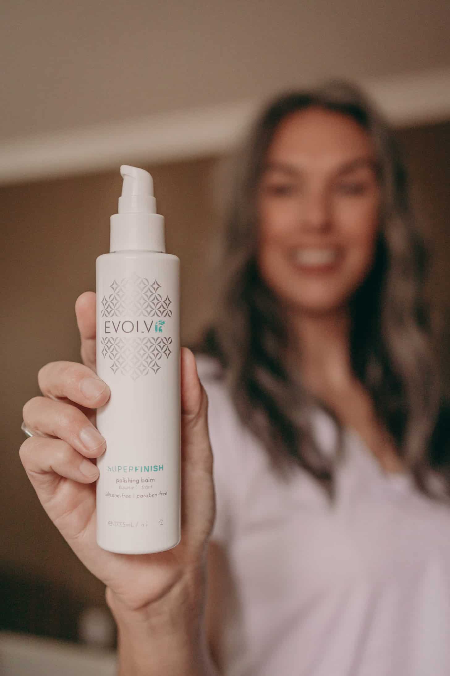 a bottle of evolvh superfinish is held up close by a slightly blurred woman in the background