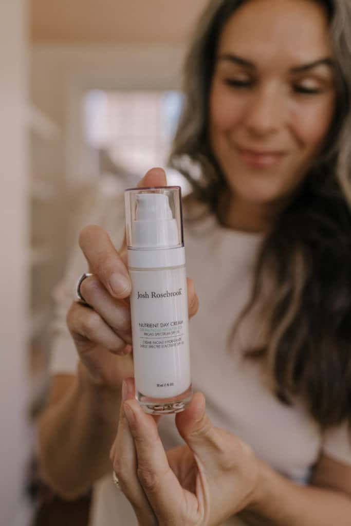 a woman with long hair holds a bottle of josh rosebrook nutrient day cream