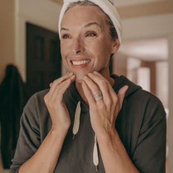 a woman in a sweatshirt applies a cosmetic mask to her face