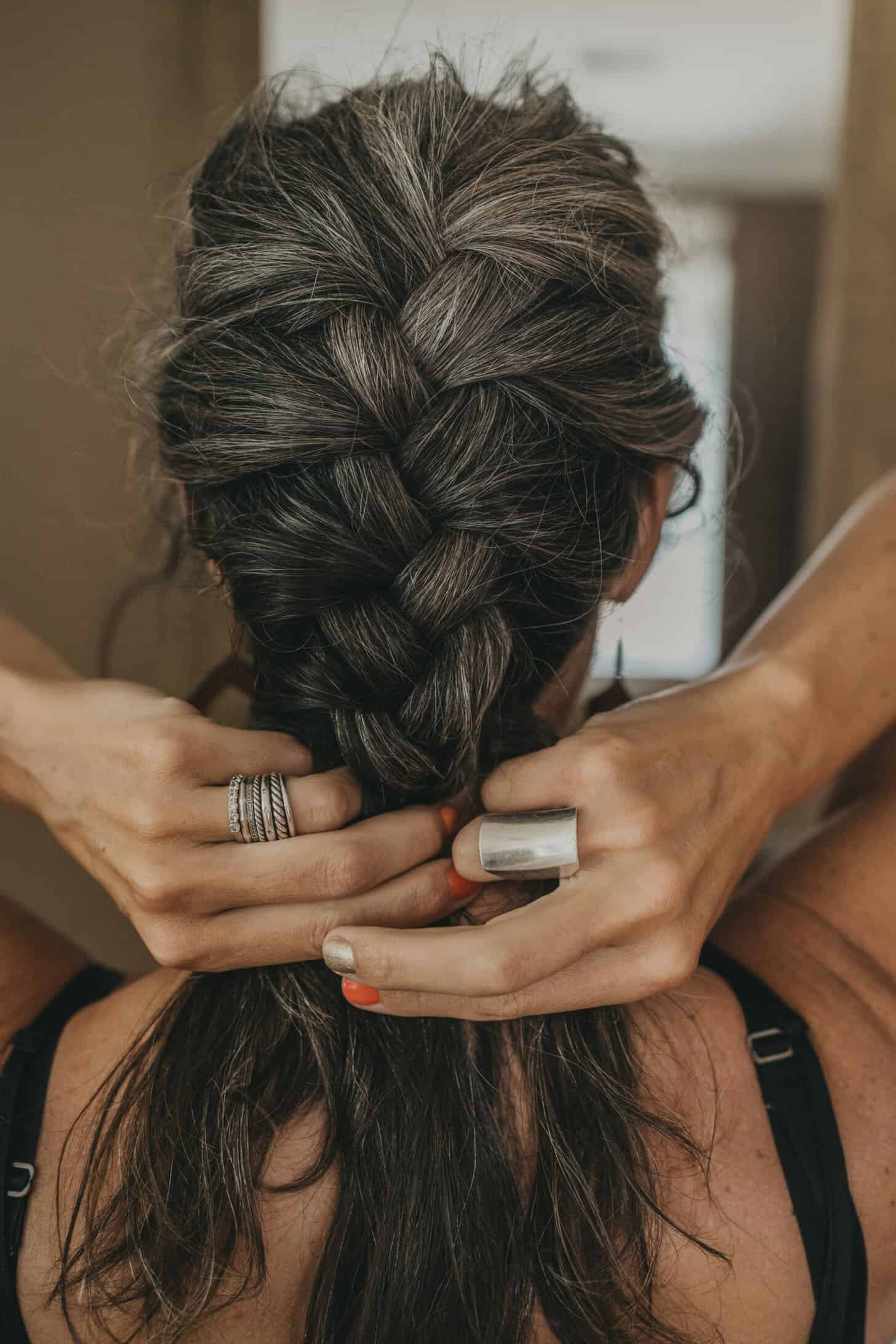 the back of a woman's head as she french braids her hair