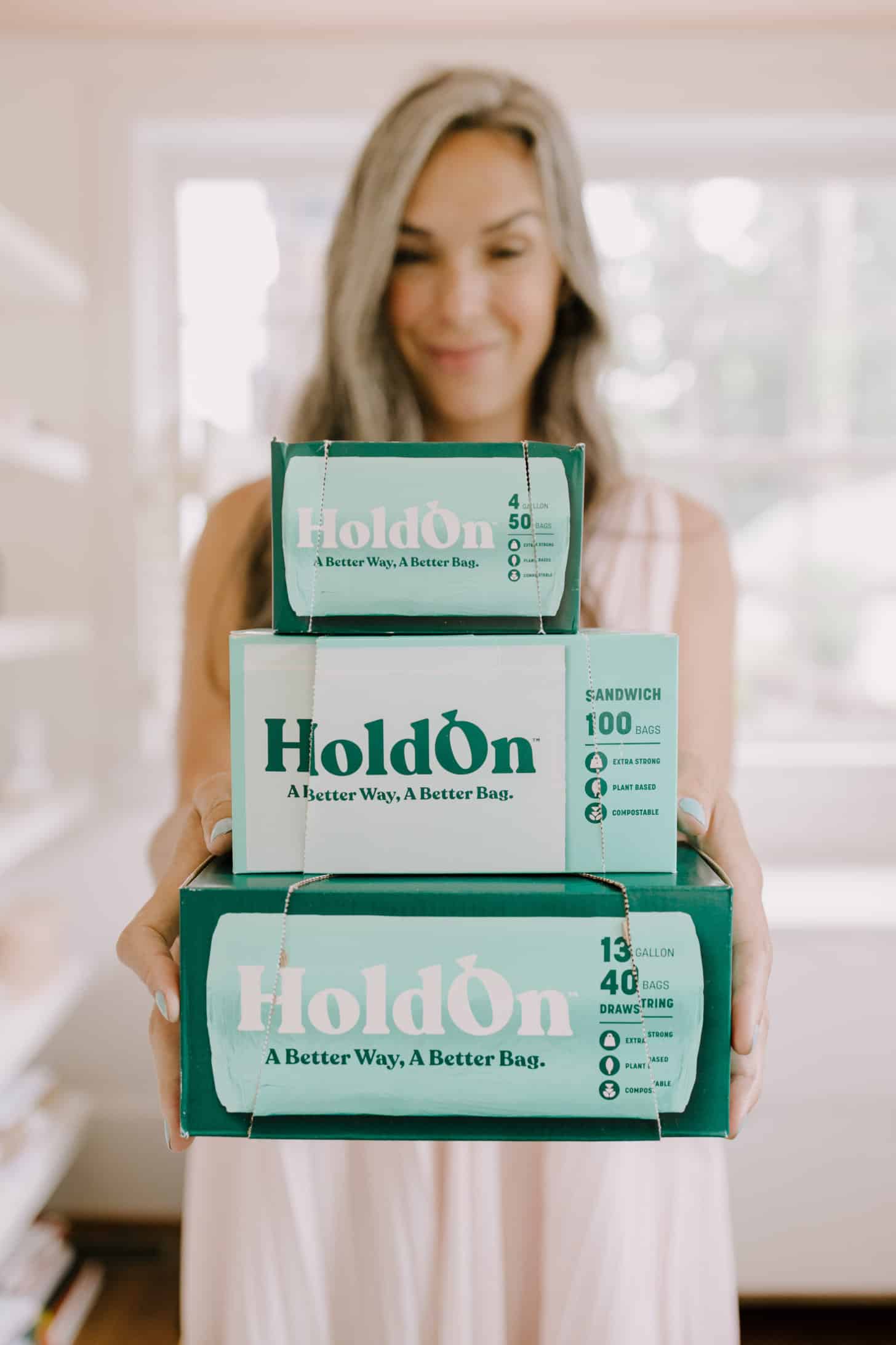 a woman holds a stack of three HoldOn compostable bags boxes up to the camera