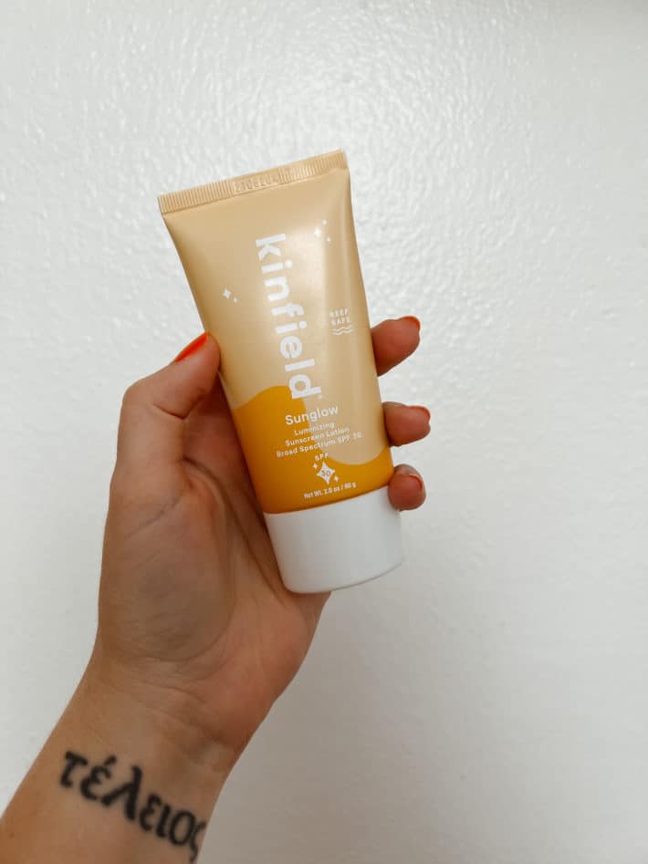 a bottle of kinfield sunglow face spf is held in a woman's hand