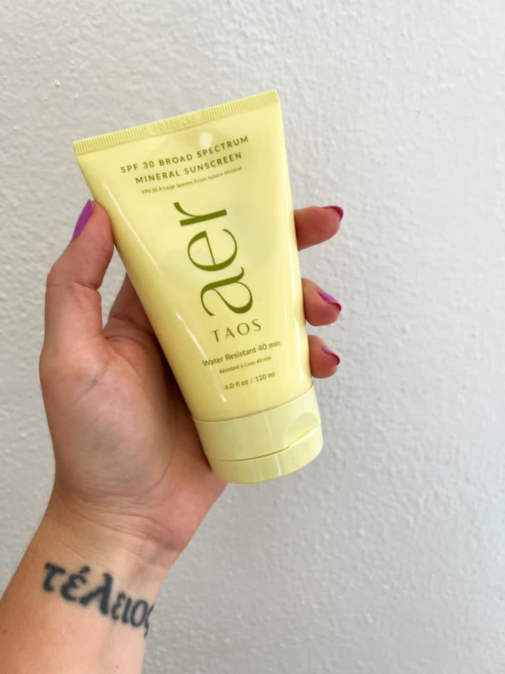 a hand holds up Taos AER SPF 30 Broad Spectrum Mineral Sunscreen.