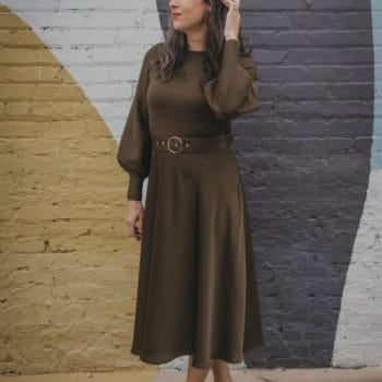 a woman wearing an olive dress stands in front of a mural