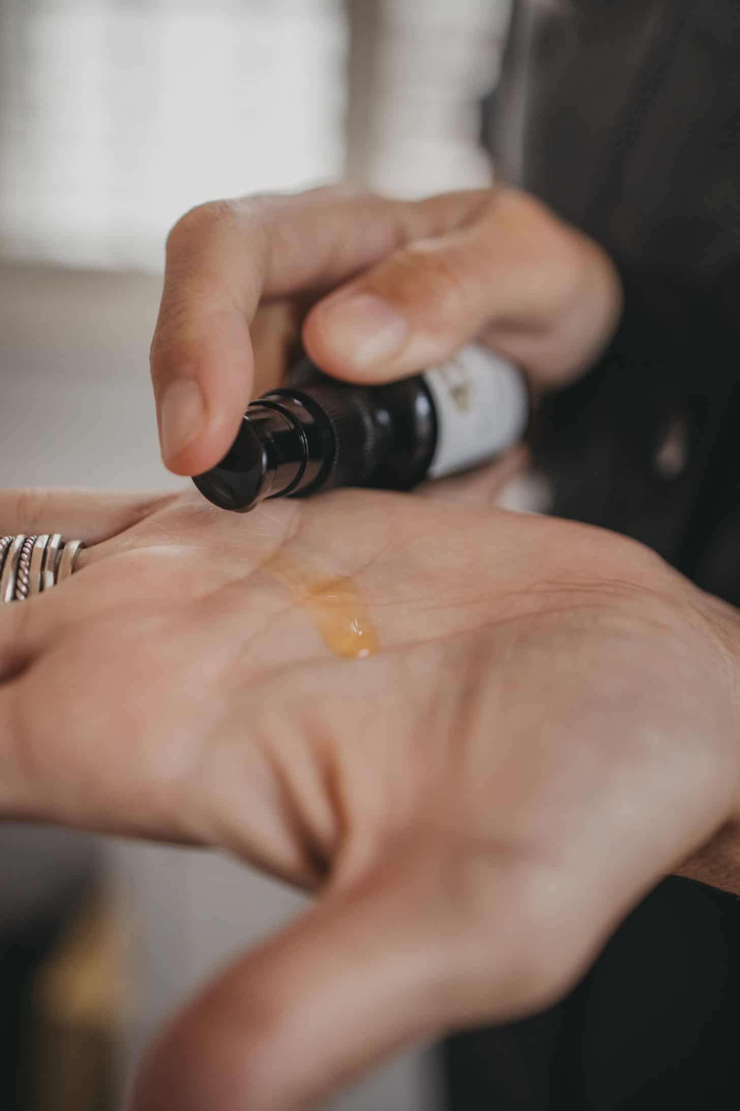a container of face serum is pumped onto the palm of a hand