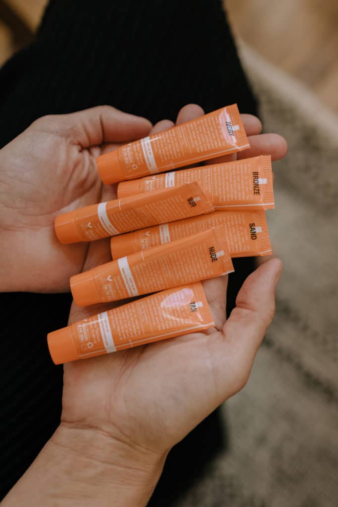 a collection of Suntegrity Impeccable Skin SPF tubes are spread out in a woman's hands