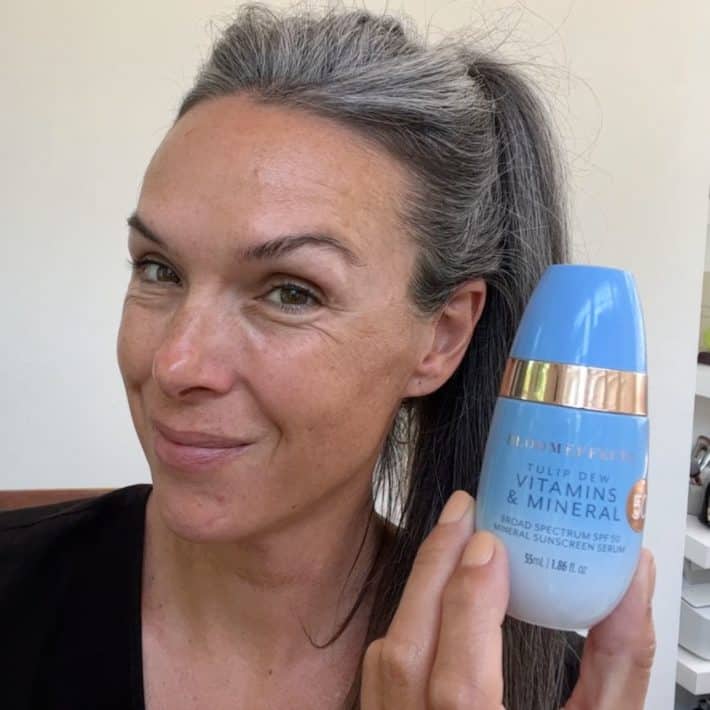 a smiling woman holds up a container of Bloomeffects tulip dew sunscreen serum