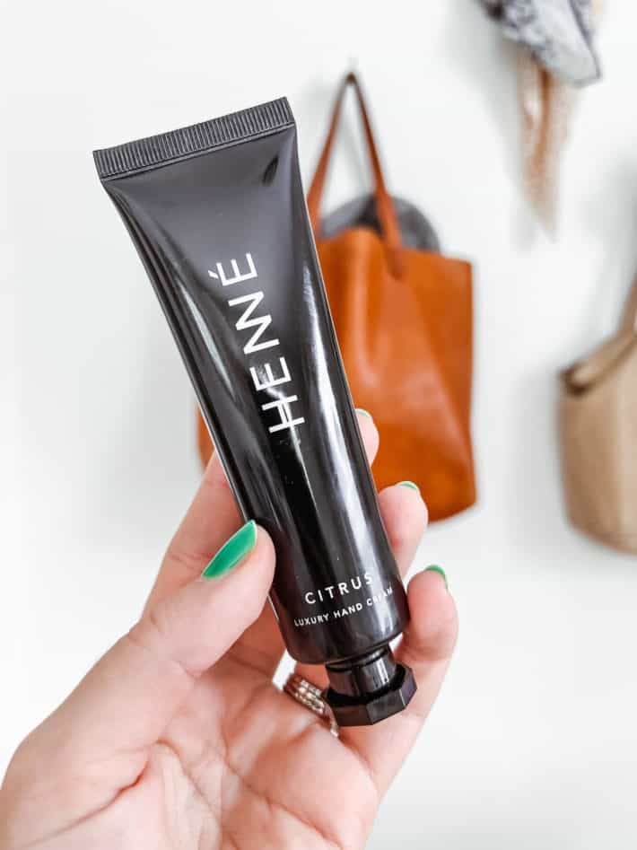 a tube of Henne luxury hand cream is held in a woman with green nail polish's hand