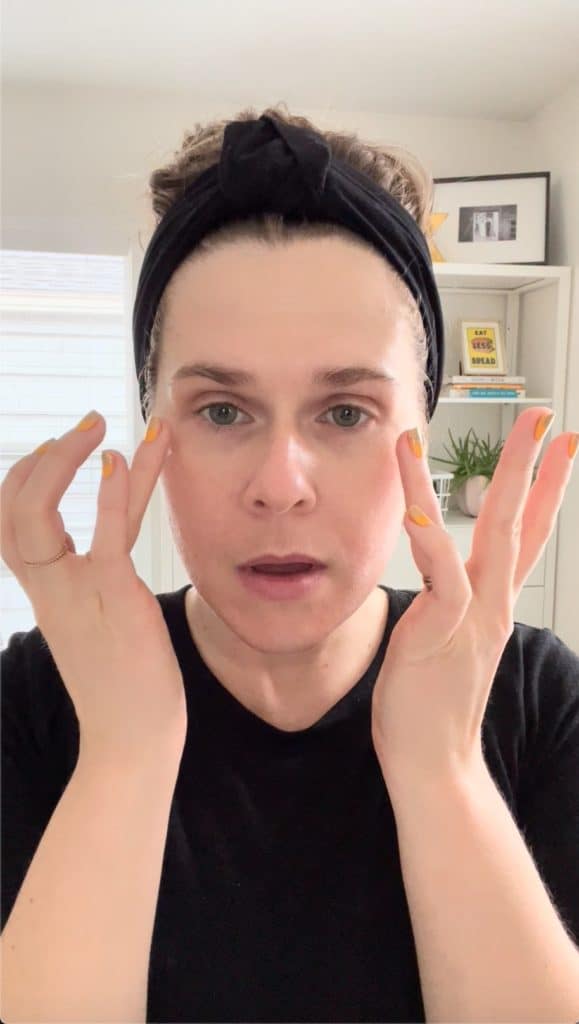 a woman applies skincare products to her face with her fingertips