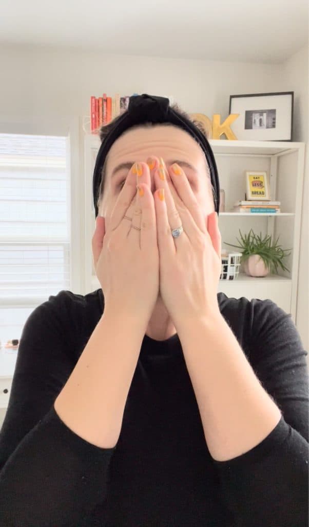 a woman applies skincare products to her face while patting her face with her hands