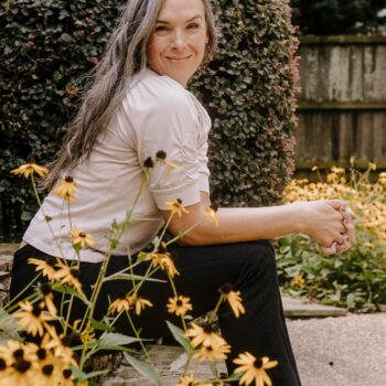 a woman smiles as she sits near black eyed susan flowers in bloom