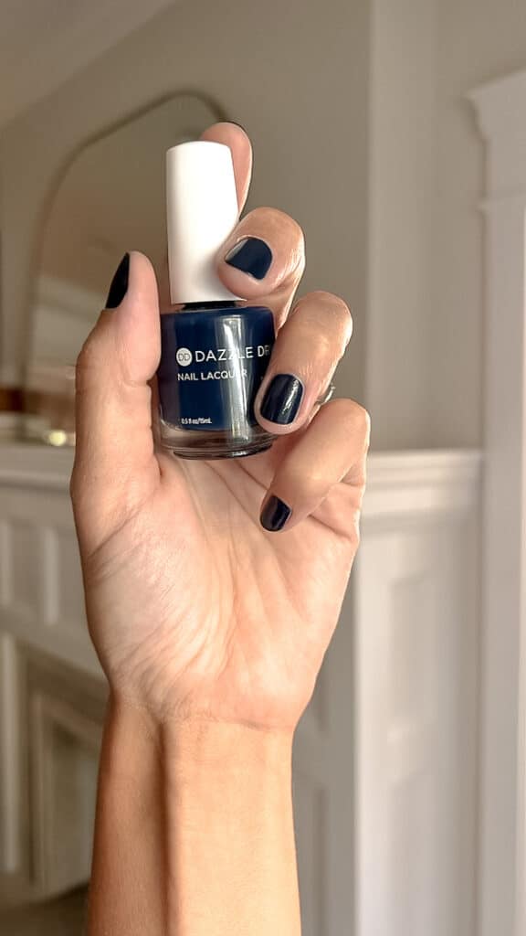 a hand holds up a bottle of dazzle dry gambit nail polish with nails painted in the same color